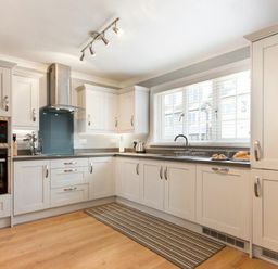 A kitchen with white cabinets stainless steel appliances a window with blinds and a striped rug on the floor at Castlewood in Bamburgh