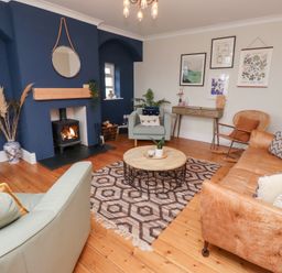 A living room with a fireplace blue accent wall armchairs a leather sofa round coffee table and wall art at Rosedale Lodge in Alnmouth
