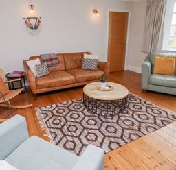 A living room with a brown leather sofa a rattan rocking chair a round coffee table and an armchair at Rosedale Lodge in Alnmouth
