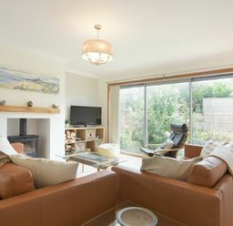 A living room with two brown sofas a glass coffee table a black armchair a television and large sliding glass doors at Spuggies Rest in Embleton