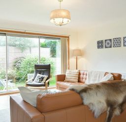 A living room with leather sofas a fur throw a lounge chair and large sliding glass doors overlooking a garden at Spuggies Rest in Embleton