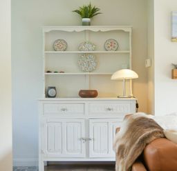 A white wooden cabinet with decorative plates and a lamp next to a brown sofa with a blanket at Spuggies Rest in Embleton