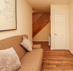 A room with a brown sofa with cushions a door wooden stairs and a framed picture of Winnie the Pooh at Stewart House in Wooler