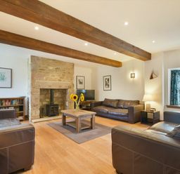 A living room with brown leather sofas a wooden coffee table with sunflowers and a stone fireplace at The Warren in Bamburgh