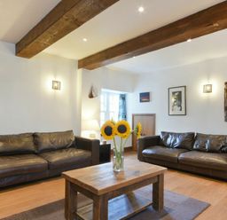 A living room with two brown leather sofas wooden beams on ceiling and a wooden coffee table with sunflowers at The Warren in Bamburgh