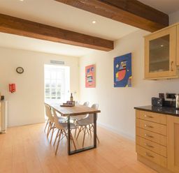 A kitchen with wooden beams wooden cabinets a dining table with chairs and colorful paintings on the wall at The Warren in Bamburgh