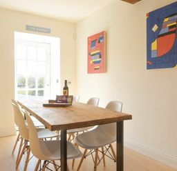 A dining room with a wooden table six white chairs and abstract paintings on the wall at The Warren in Bamburgh