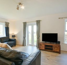 A living room with leather sofas a wooden TV stand and windows at Coastal Plaice in Beadnell