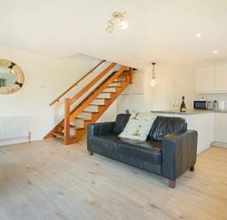 A living area with a black sofa two cushions wooden stairs and a kitchen with white cabinets at Coastal Plaice in Beadnell