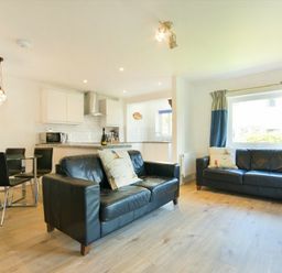 A living room with two black leather sofas and a dining table with black chairs in an open plan kitchen area at Coastal Plaice in Beadnell