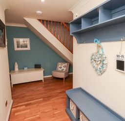 A hallway with wooden flooring a blue shelf a white bench a chair under stairs and decorations at The Wynd in Bamburgh