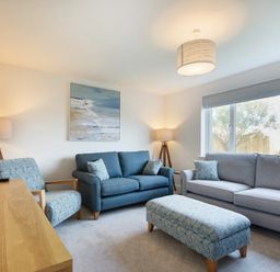 A living room with two sofas one armchair an ottoman wooden TV stand lamps and a large window at Luna Tide in Seahouses