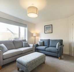 A living room with two sofas a patterned ottoman a floor lamp and a framed picture at Luna Tide in Seahouses