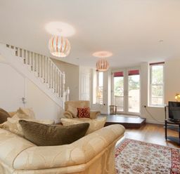 A living room with sofas, armchair, rug, TV on stand, staircase, and glass doors at The Old Concert Room in Alnmouth