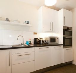 A kitchen with white cabinets a sink microwave toaster and oven at The Old Concert Room in Alnmouth