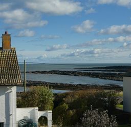 Sea view with rocky shore and clouds above with parts of white houses and garden bushes nearby at Coast View in Beadnell
