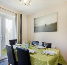 A dining room with a table set for six people and glass doors leading outside at Coast View in Beadnell