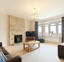 A living room with a stone fireplace a wooden coffee table two sofas a television and windows with curtains at Bradacar in Seahouses