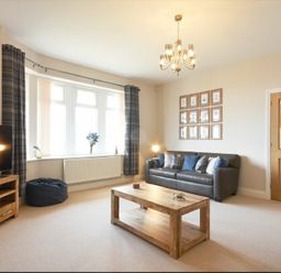 A living room with a leather sofa and wooden coffee table near a window with curtains and a television on a wooden stand at Bradacar in Seahouses