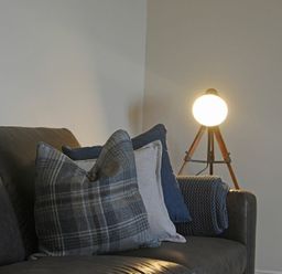 A sofa with cushions and a blanket next to a tripod floor lamp at Bradacar in Seahouses