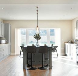 A kitchen with grey cabinets a central island with stools and large windows at Bradacar in Seahouses
