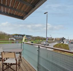 A balcony with two chairs and a table overlooking a street with a statue on a rock and a building in the background at Castle View at the Viking in Seahouses