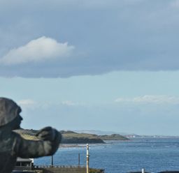 A coastal view with a statue in the foreground and ocean with hills in the background at Castle View at the Viking in Seahouses