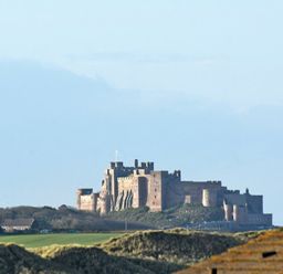 A large stone castle on a grassy hill with trees and buildings nearby at Castle View at the Viking in Seahouses