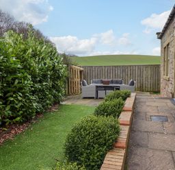 An outdoor patio area with seating and table beside a stone building and hedge at The Old Stables in Bamburgh