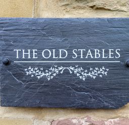 A black stone plaque with the text the old stables and a decorative floral design on a stone wall at The Old Stables in Bamburgh