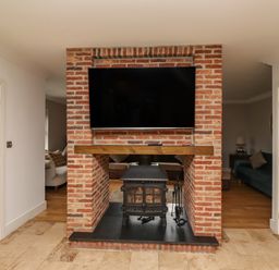 A brick fireplace with a wood stove and a mounted TV above it between two wooden doors at The Old Stables in Bamburgh