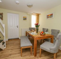A dining room with a wooden table set for a meal with gray chairs and a bench near stairs at Cove Street Cottage in Weymouth