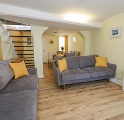 A living room with two gray sofas with yellow cushions and a dining area with a wooden table and chairs at Cove Street Cottage in Weymouth