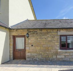 An exterior view of a stone and plaster building with a wooden door and window at Dairymaid's Cottage in Amble