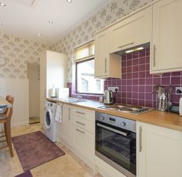 A kitchen with cream cabinets purple tiled backsplash and wooden countertops at Dairyman's Cottage in Amble