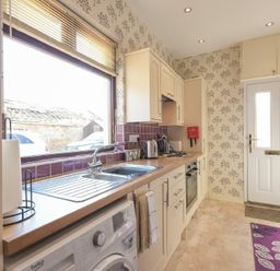A kitchen with white cabinets a stainless steel sink a washing machine and a white door at Dairyman's Cottage in Amble