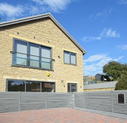 A stone house with gray framed windows and a gray wooden fence around a paved driveway at Riverview (Alnmouth) in Alnmouth