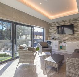 A sitting area with rattan chairs and a table next to sliding glass doors and a wall-mounted TV at Riverview Alnmouth in Alnmouth