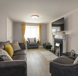 A living room with gray sofas yellow curtains and a wall-mounted TV at Coastal View in Seahouses