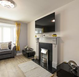 A living room with an armchair yellow curtains a fireplace and a wall mounted TV at Coastal View in Seahouses