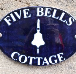 An oval dark blue sign with white text reading Five Bells Cottage mounted on a stone wall