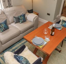 A seating area with a beige sofa and two chairs around a wooden dining table set with plates glasses and a bottle at Five Bells Cottage in Alnmouth