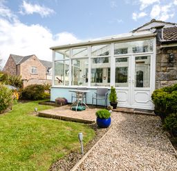 A patio with table and chairs next to a glass conservatory and garden path at Palmers Rest in Beadnell
