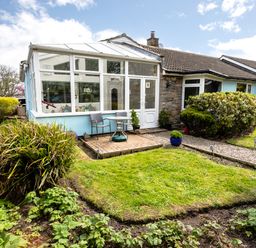 A garden with shrubs and a conservatory attached to a house at Palmers Rest in Beadnell