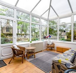 A sunroom with two wicker chairs a small table a couch with patterned cover a rug and a telescope at Palmers Rest in Beadnell