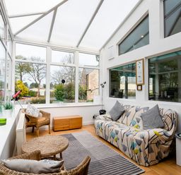 A sunroom with wicker chairs a sofa with patterned cover and large windows at Palmers Rest in Beadnell