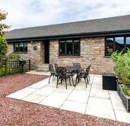 A stone exterior house with black metal outdoor table and chairs on a stone patio at Polished Pebble in Beadnell
