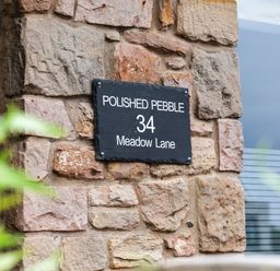 A stone wall with a black sign reading polished pebble 34 meadow lane with a window nearby at Polished Pebble in Beadnell