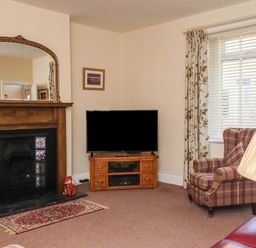 A living room with a fireplace mirror and television beside a plaid armchair at Creel Cottage Blackwood Street in Amble