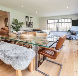 A dining area with glass table and chairs with a living room area with armchairs and a TV at Willow in Beadnell